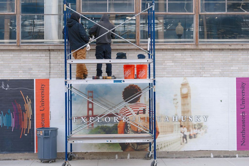 Workers on scaffolding painting a wall mural with 'Arlo & Beauty' text and pastel panels