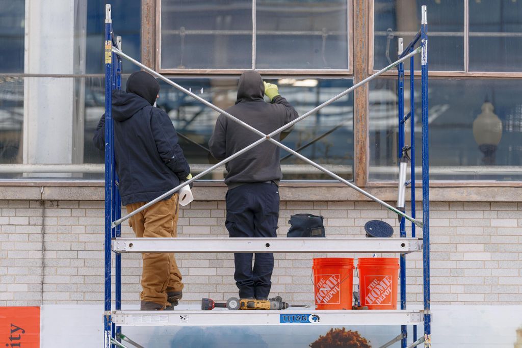Two workers on a blue scaffold painting a building exterior, with buckets and tools below.
