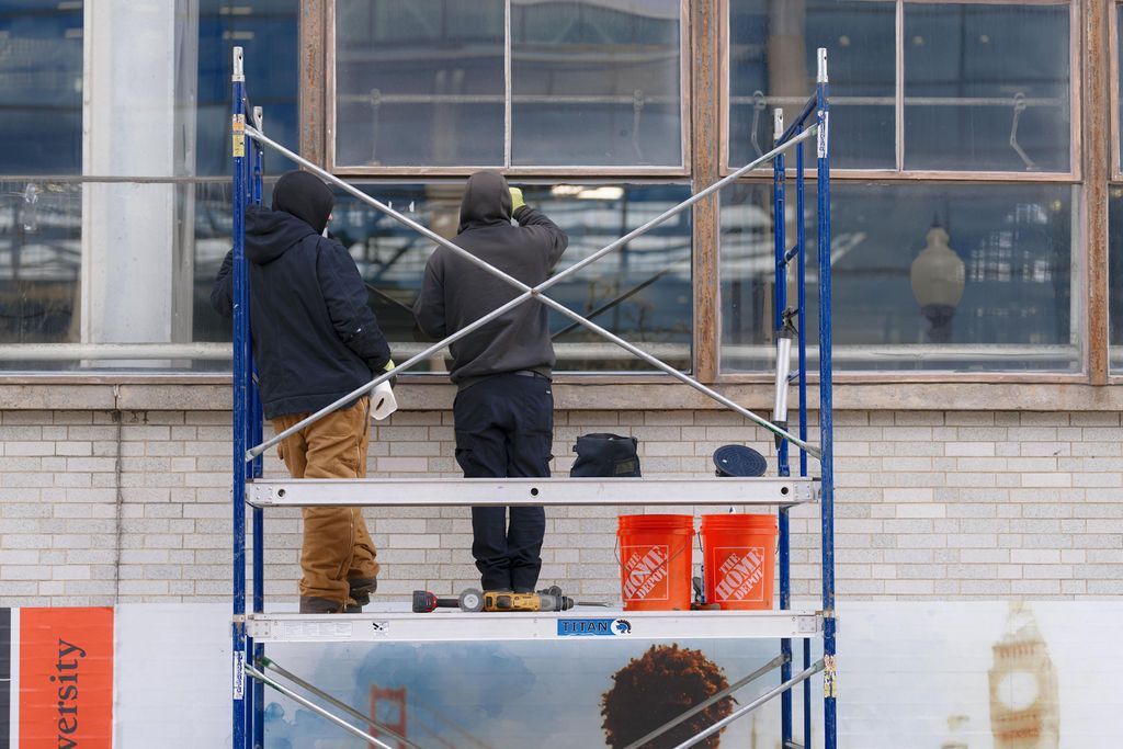 Two workers on a scaffold painting a building’s exterior windows and brick wall