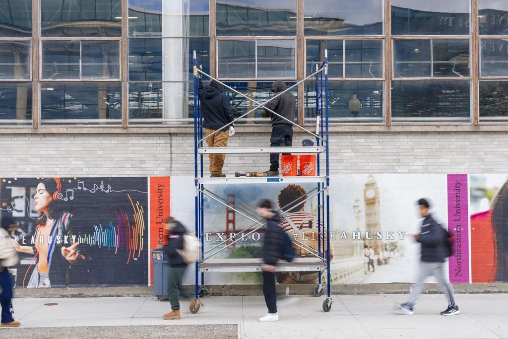 People working on a blue scaffold in front of a building, with pedestrians passing by.