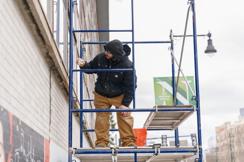 Worker on a scaffold painting a brick wall beside a street.
