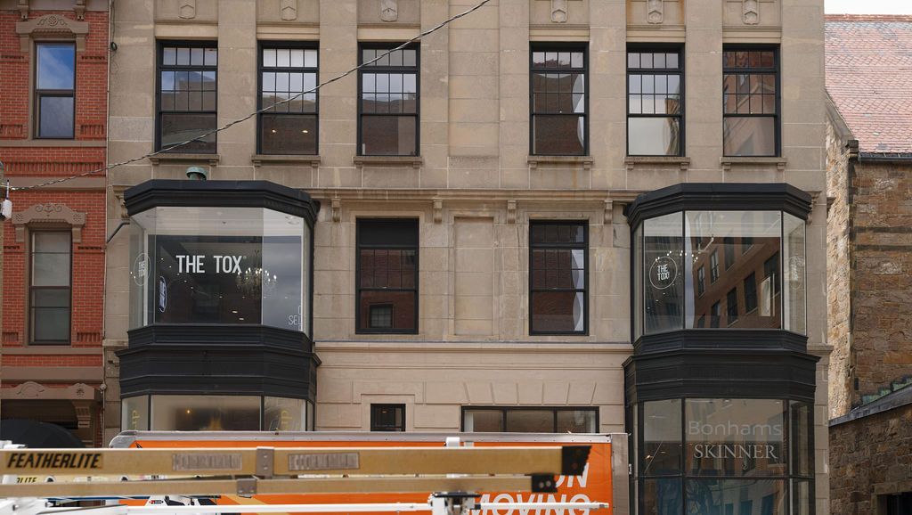 Street-level view of a brick building with storefronts and a passing orange bus in front