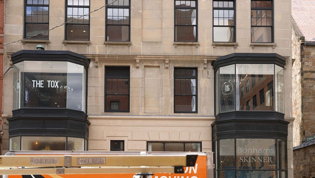 Storefronts in a stone building with a white-and-orange truck parked in front.