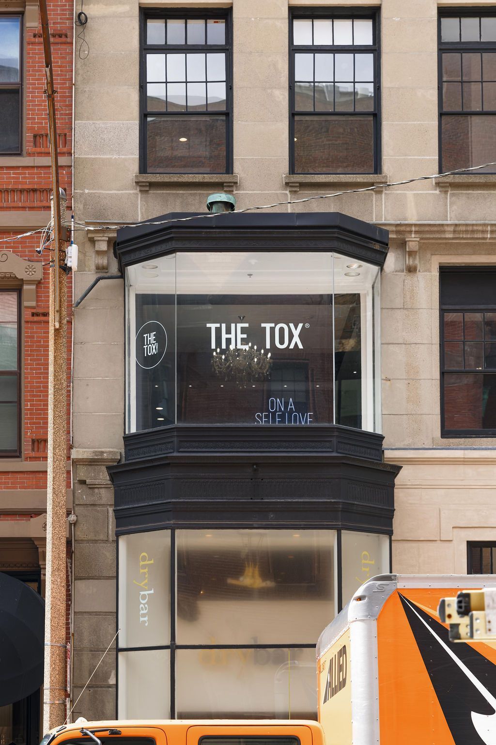 Storefront with a black bay window sign reading 'THE TOX' on a brick building, partly blocked by a truck