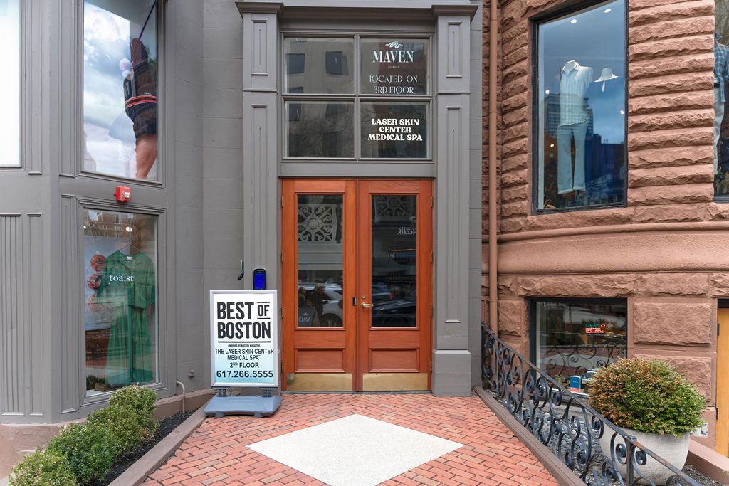 Storefront entrance with wooden double doors, gray and brick exterior, and a small 'Best by Design' sign.