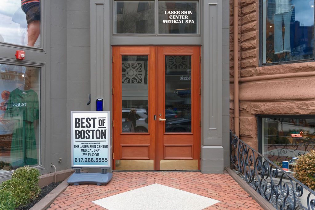 Storefront entrance with orange double doors, 'Best of Boston' sign, and sidewalk seating outside.