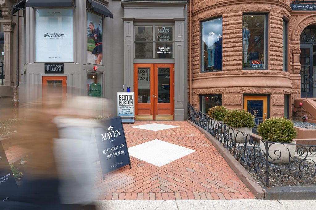 Brick storefront with orange double doors and a chalkboard sign on a brick sidewalk, blurred passerby in foreground