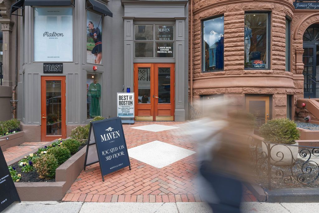 Shopfronts with orange doors and a sidewalk café sign in a brick-lined downtown street.