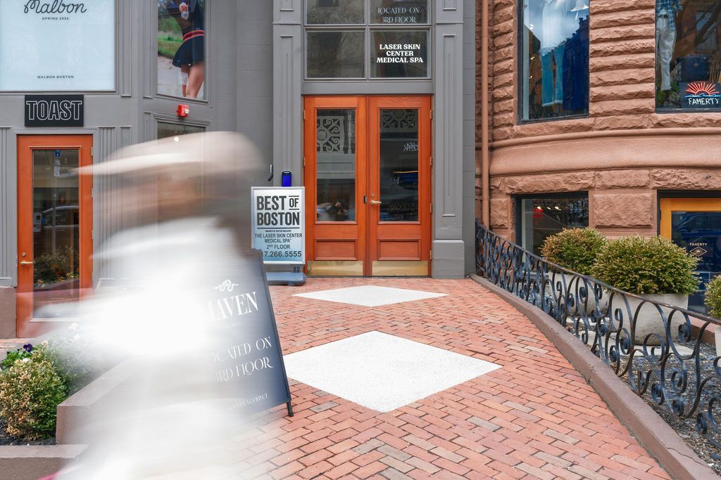 Brick storefront with orange doors, a cobblestone walkway, and a blurred pedestrian passing by