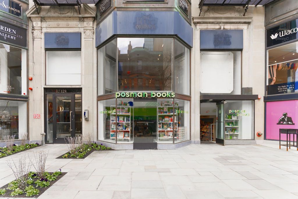 Entrance of a Sainsbury’s store in a modern shopping plaza with glass facade and planters