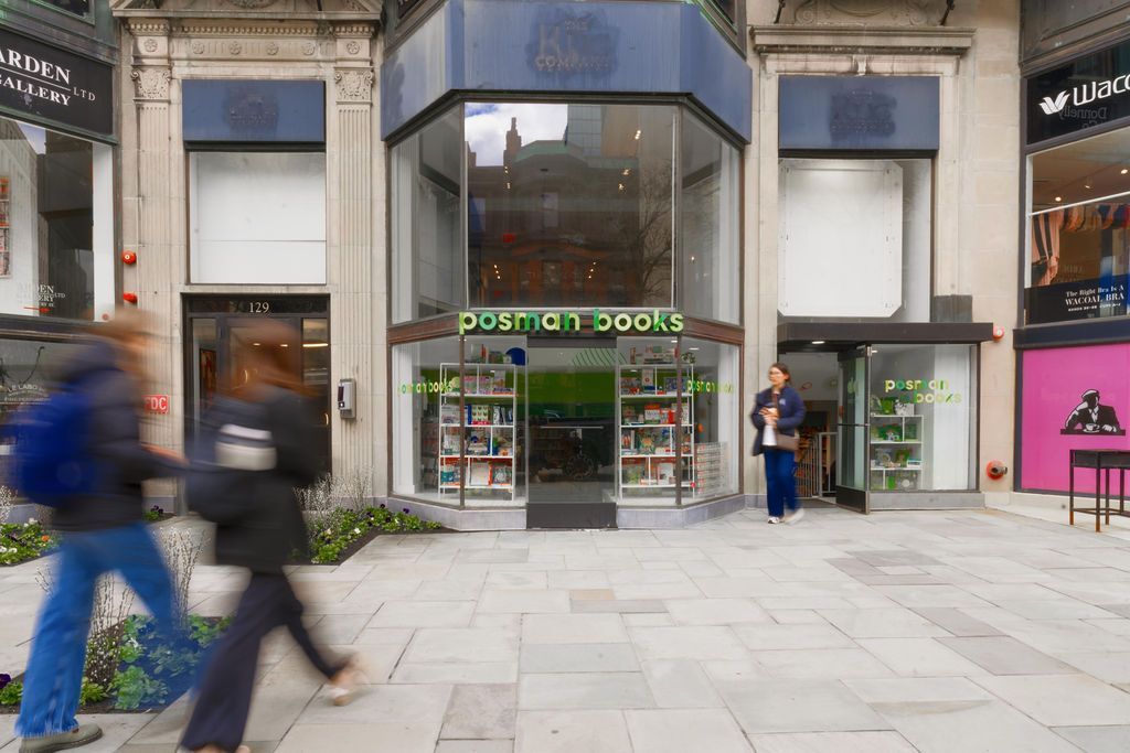 Storefront with green 'postman books' sign, two people outside, and pedestrians blurred in front on a city street.