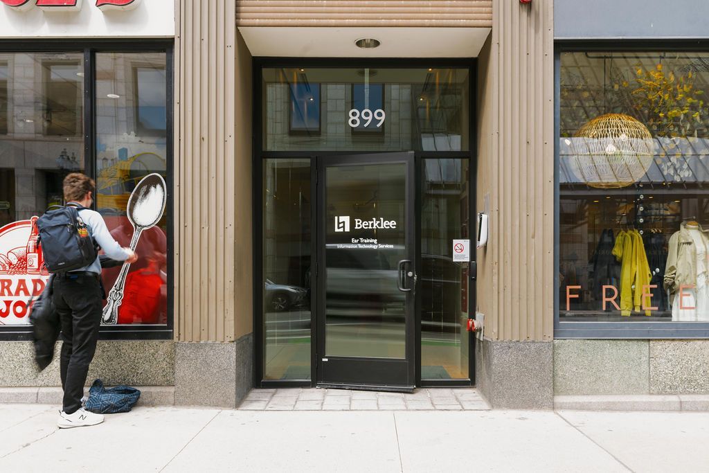 Person spraying windows outside a storefront entrance on a city sidewalk.