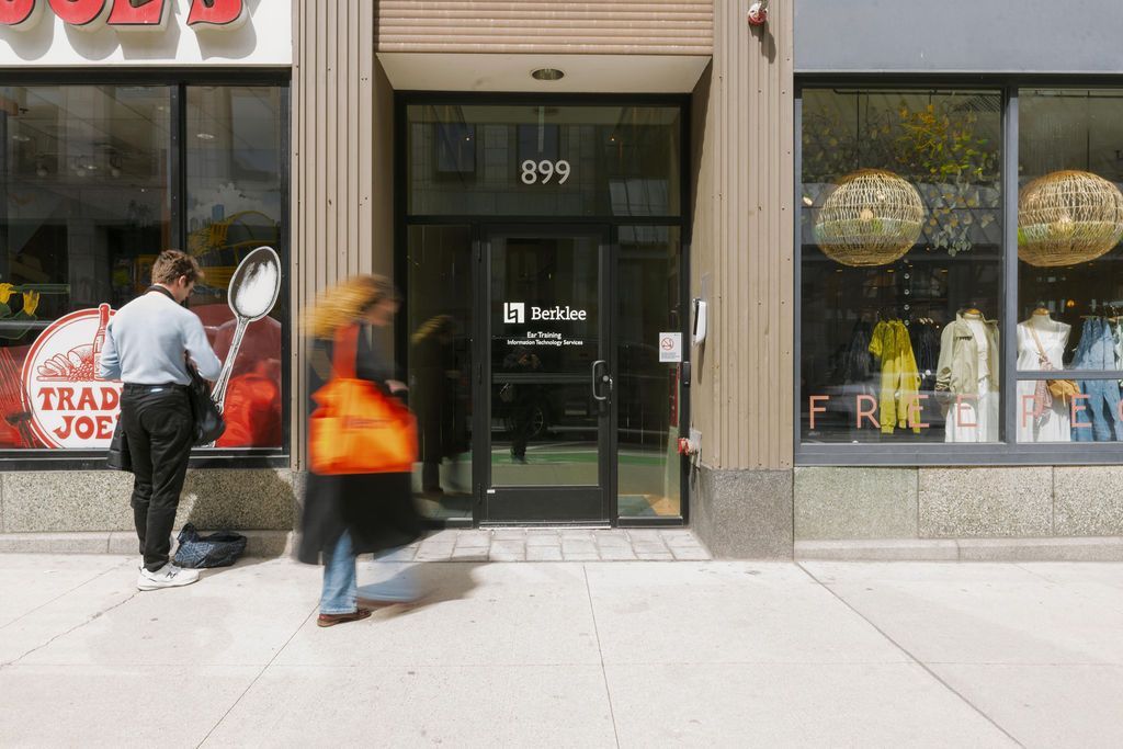 Two people walking past a storefront with a black door and display windows on a city sidewalk