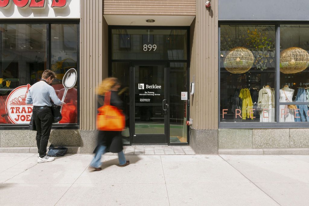 People walking past a storefront with a glass door and window displays on a city sidewalk