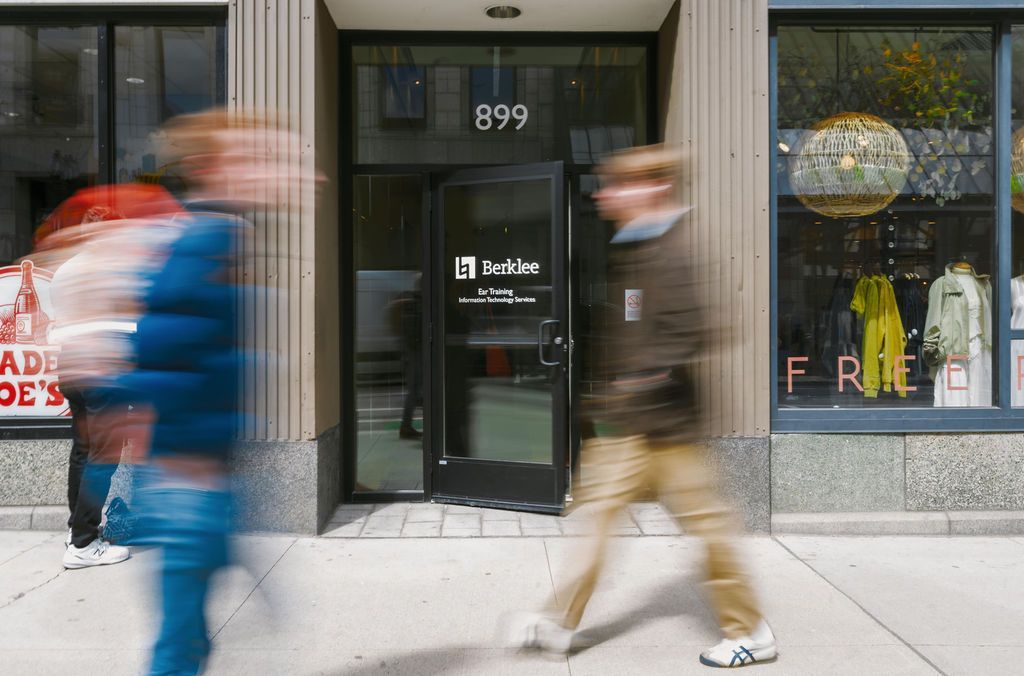Blurred pedestrians passing a storefront entrance with mannequins in the window and the number 899 above the door