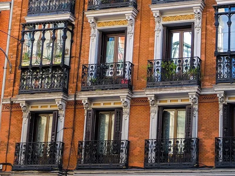 The orange brick facade of a building featuring multiple windows, decorative black iron balconies, and ornate detailing.
