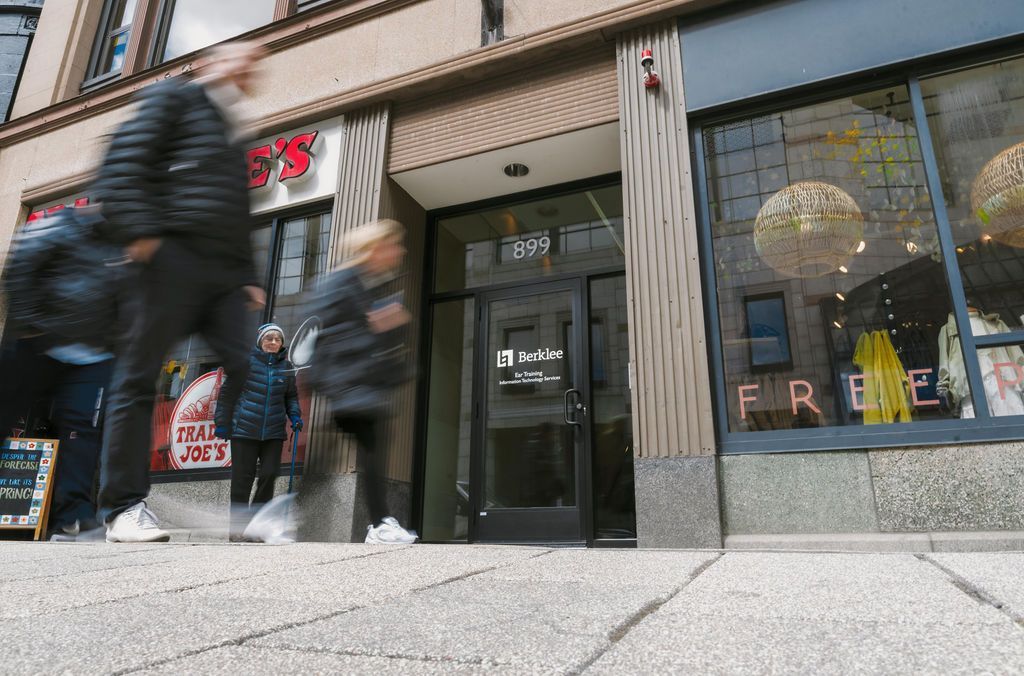People walking past a storefront with large windows and a glass door on a city sidewalk