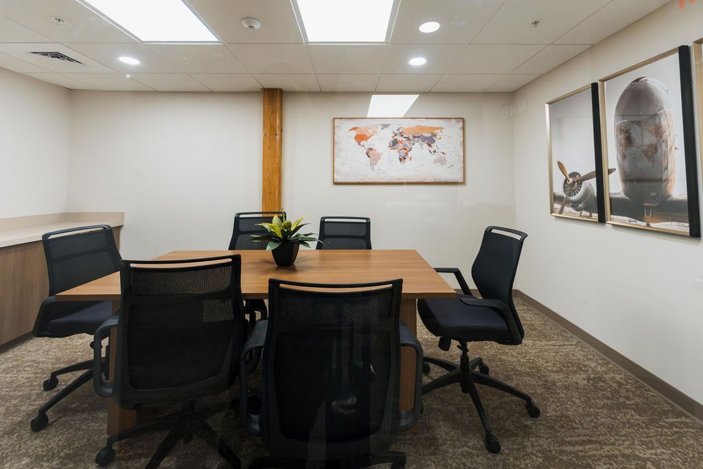 Empty conference room with a wooden table, black office chairs, and wall art on white walls