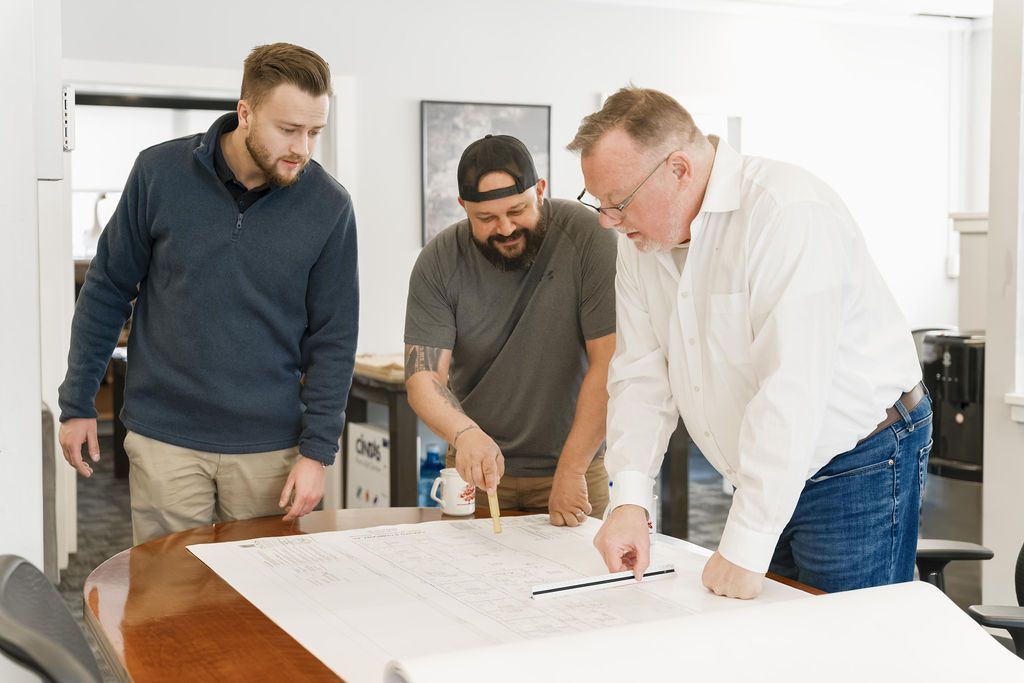 Three people reviewing blueprints together at a table in a bright office