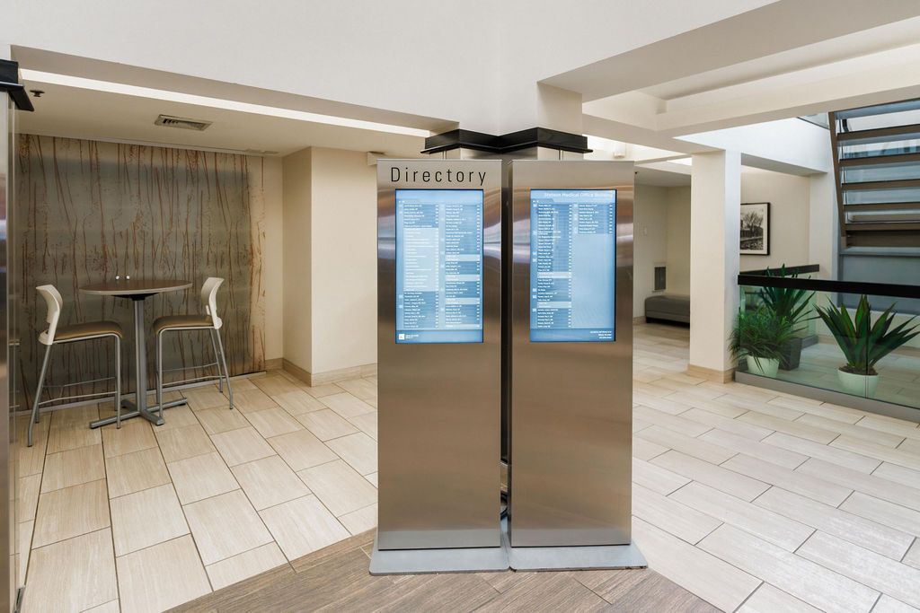 Two stainless steel elevator doors in a bright lobby with seating and plants nearby