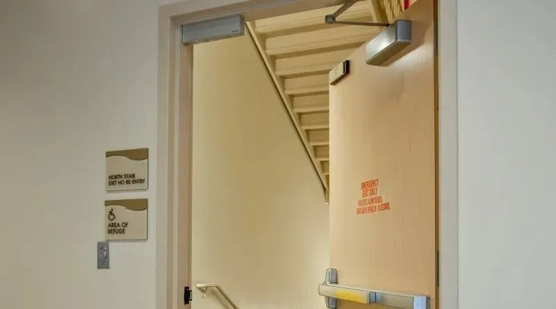 An open stairwell door with an emergency exit sign and disability signage on the adjacent wall.