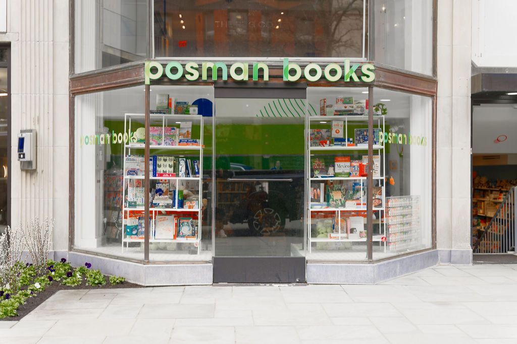 Storefront of Posman Books with large glass windows and a green sign, displaying books inside.