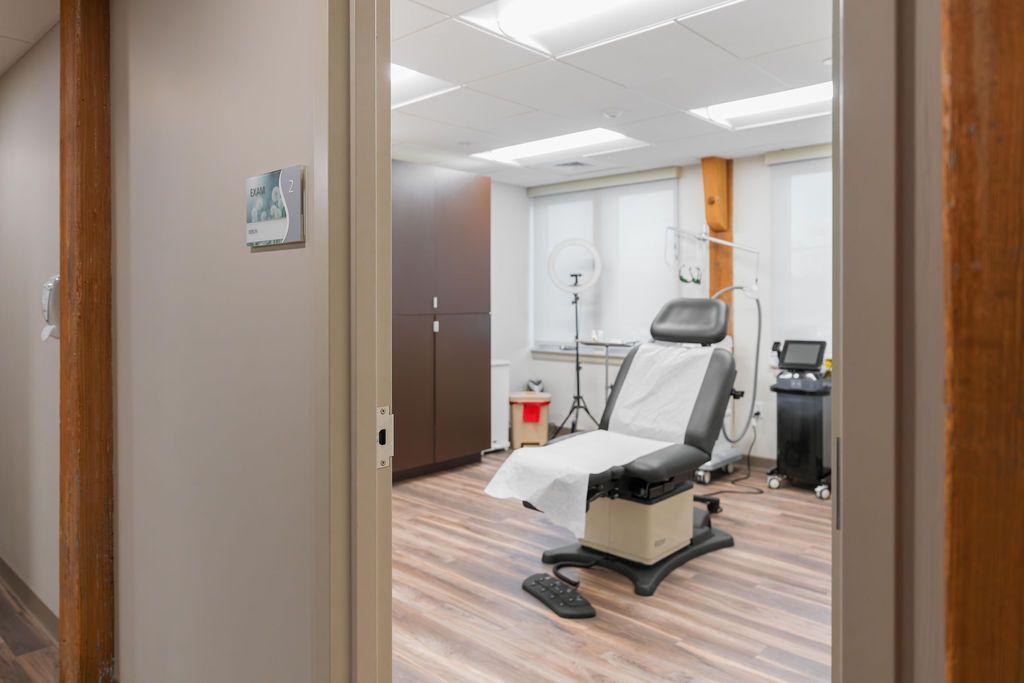 Exam room with a padded treatment chair, medical equipment, and wood flooring.
