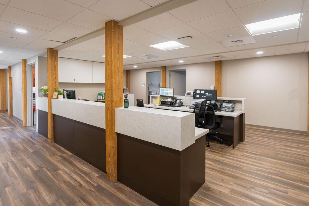 Modern office reception area with white counter, wood floor, and ceiling lights