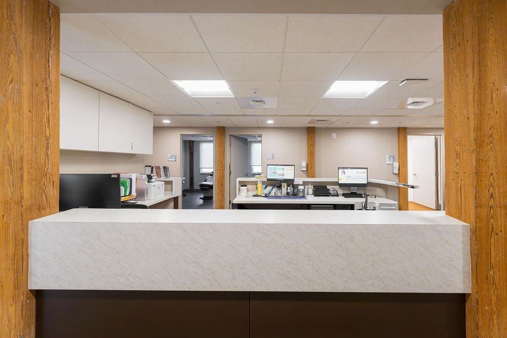 Hospital reception desk and waiting area viewed through a large opening, with white counters and fluorescent lights.