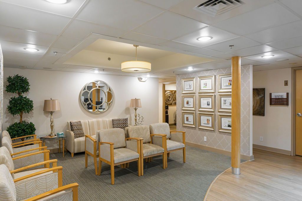 Bright waiting room with beige chairs, wall art, plants, and a reception area under soft lighting