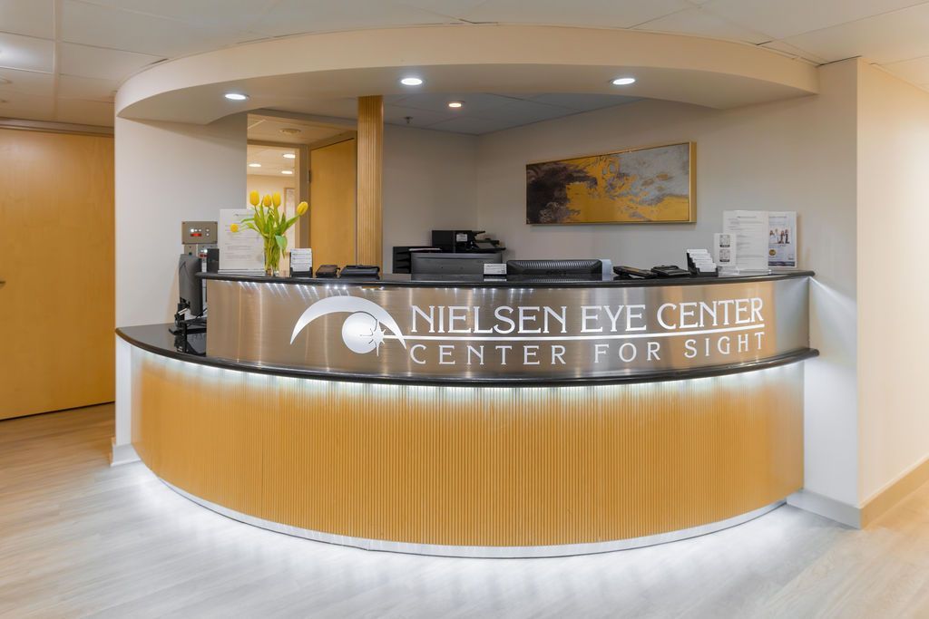 Modern eye center reception desk with curved wood front and illuminated sign in a bright lobby