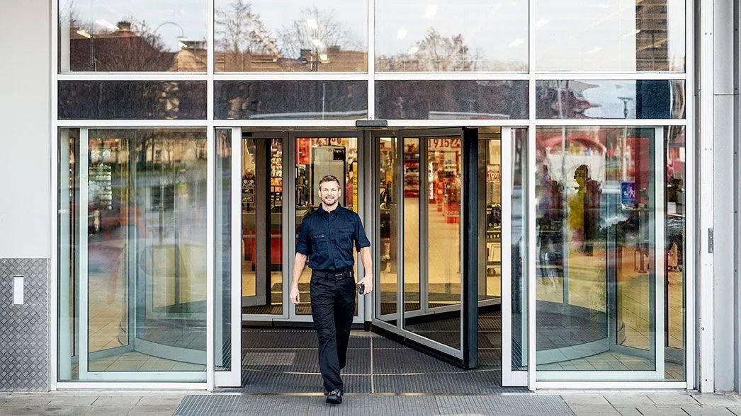 A person in a dark uniform walking through a revolving glass door entrance of a building.