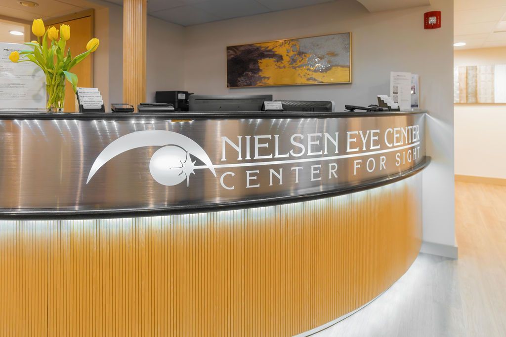 Nielsen Eye Center reception desk with brushed metal front and yellow flowers in a modern lobby