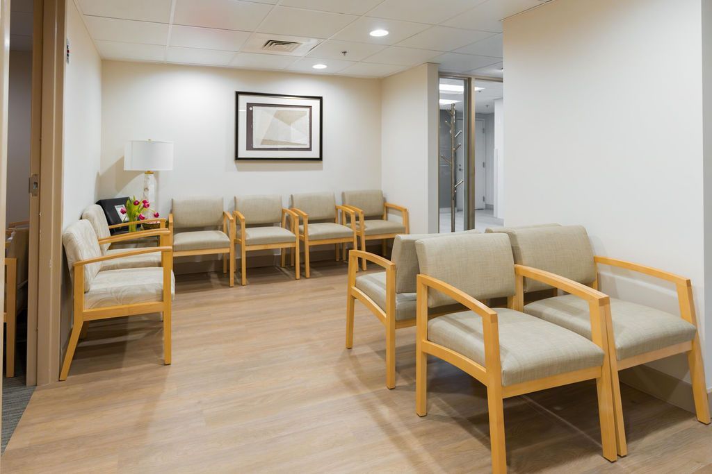Empty waiting room with beige chairs, wood flooring, and framed wall art
