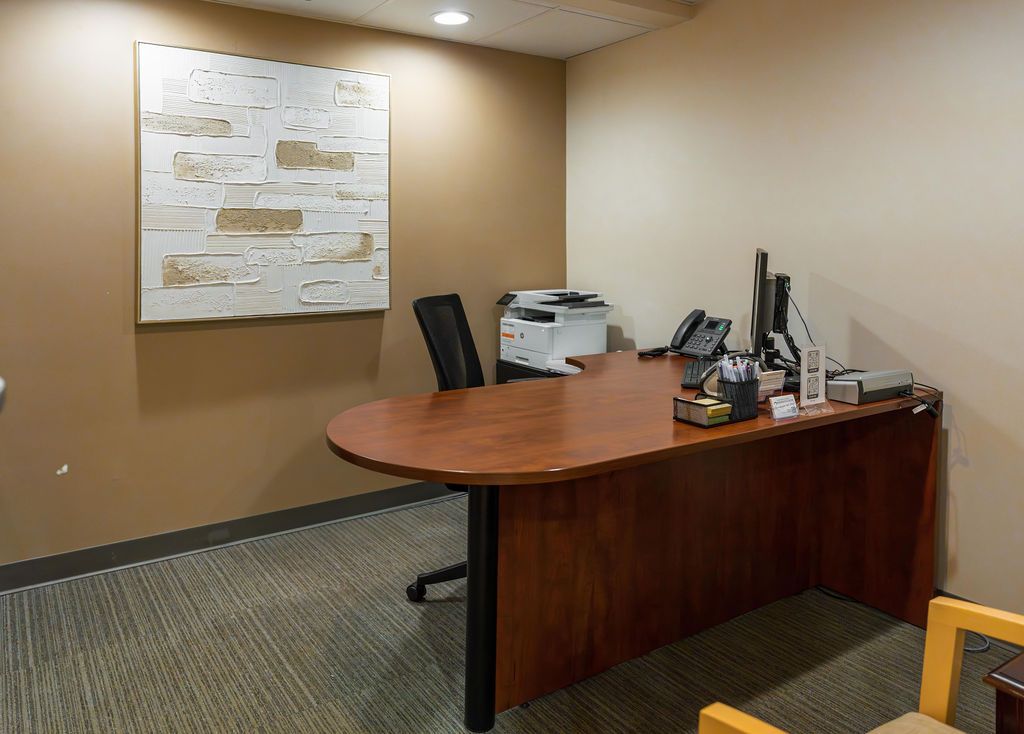 Small office with wooden desk, printer, computer monitors, and a wall map in a beige room.