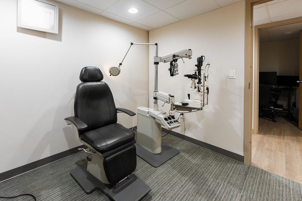 Exam room with black exam chair, wall-mounted diagnostic tools, and a floor lamp