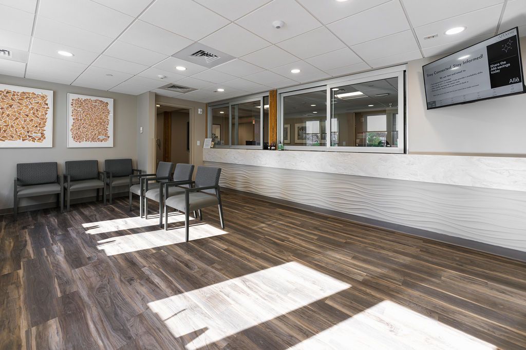 Empty modern waiting room with black chairs, wood-look floor, and a reception counter under bright lights