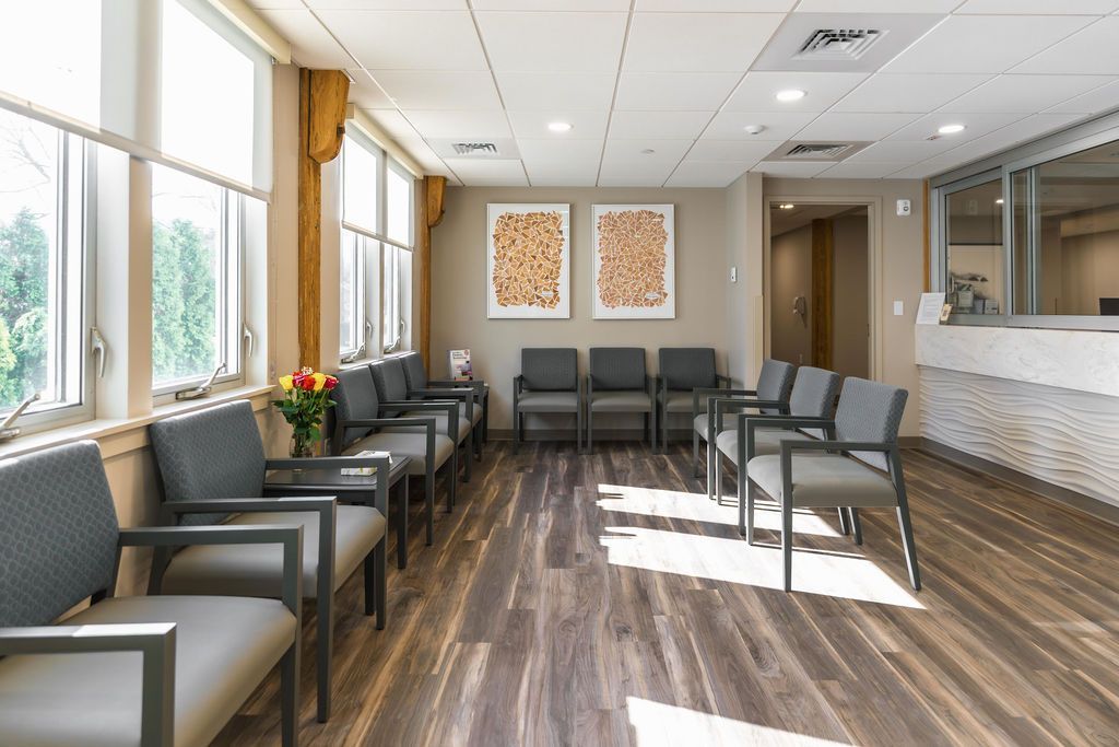 Bright waiting room with gray chairs, large windows, wood floor, and reception desk