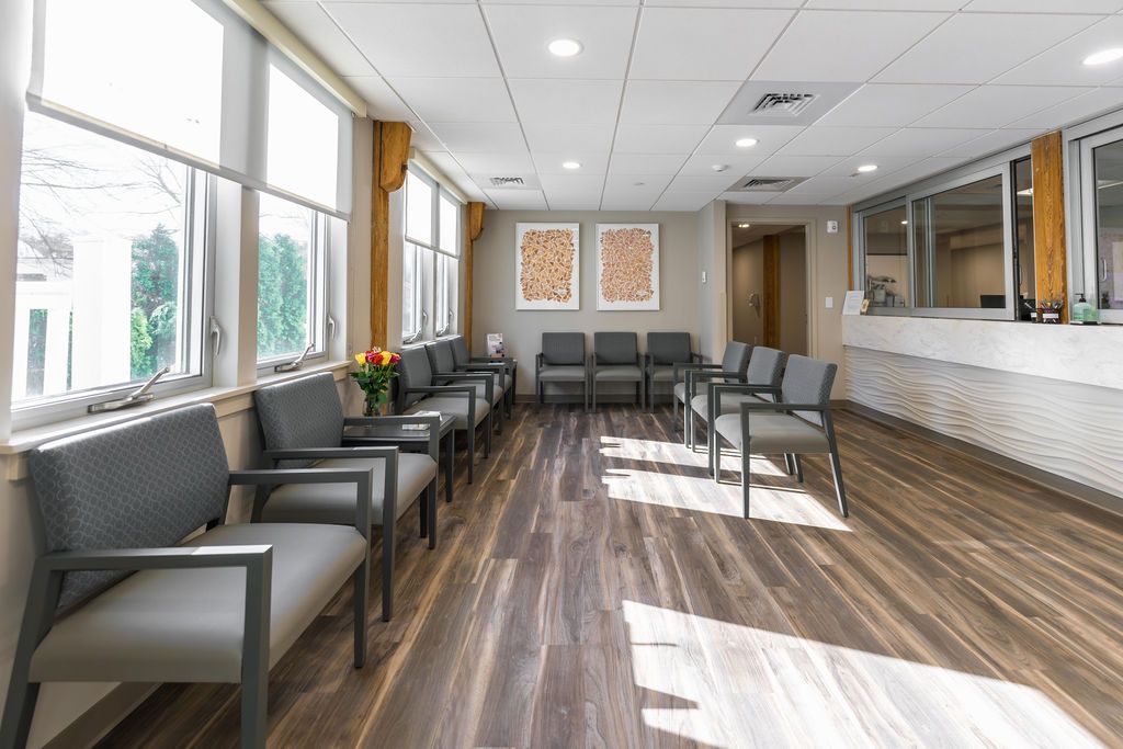 Bright waiting room with gray chairs, wood flooring, large windows, and a reception counter.