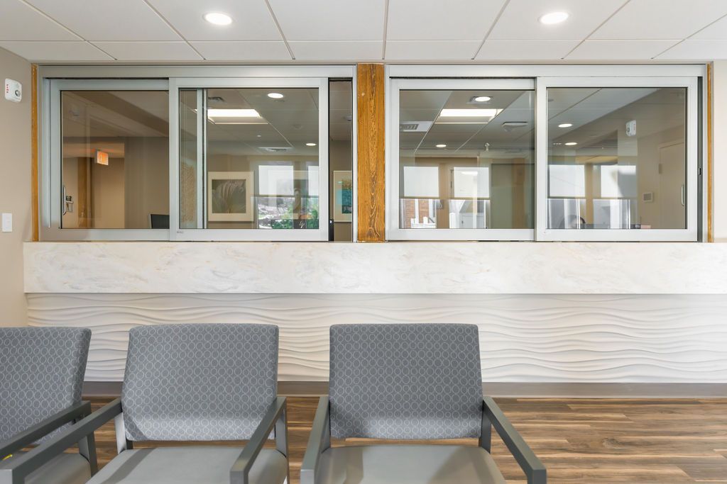 Waiting area with gray chairs facing a large interior windowed service counter