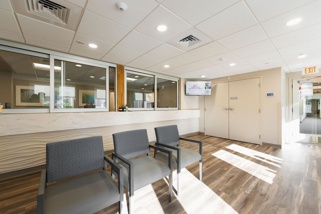 Empty waiting room with chairs, wood floor, wall windows, and bright sunlight streaming in