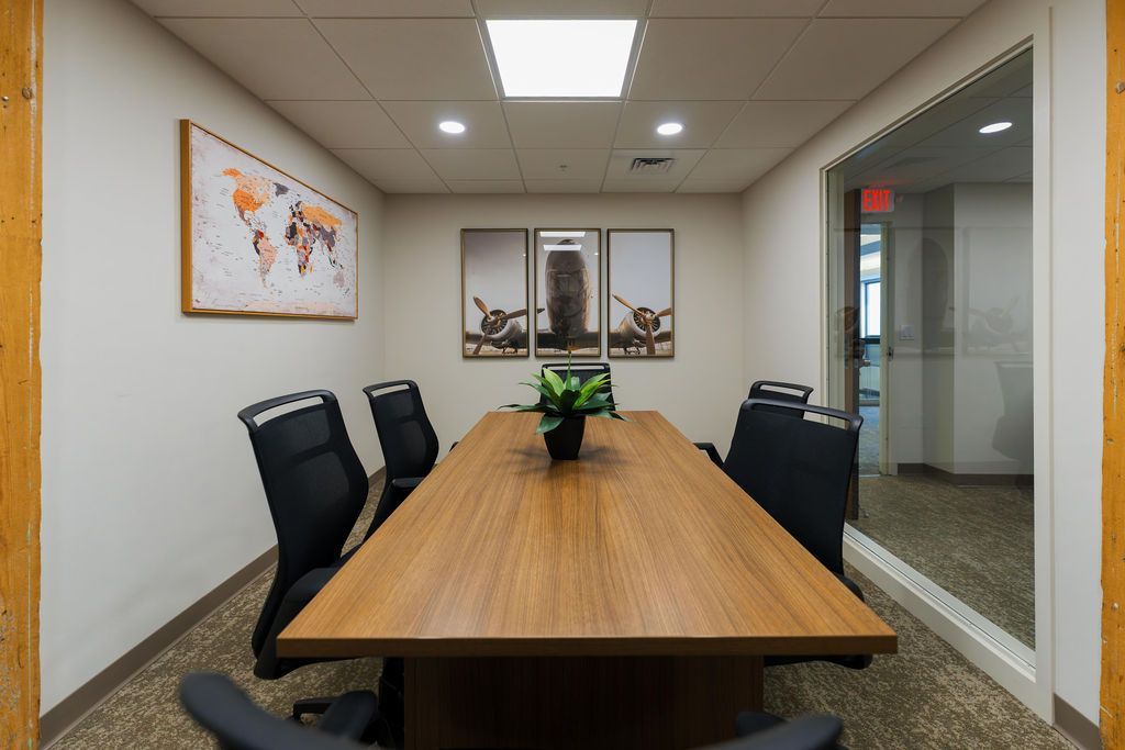 Empty conference room with long wooden table, black chairs, wall map, and glass partition.