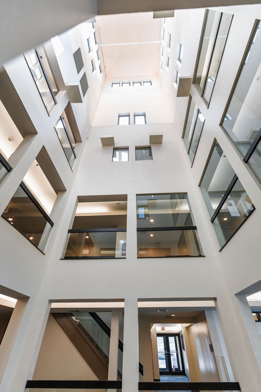 Tall modern atrium with white walls, glass railings, and multiple floors looking upward