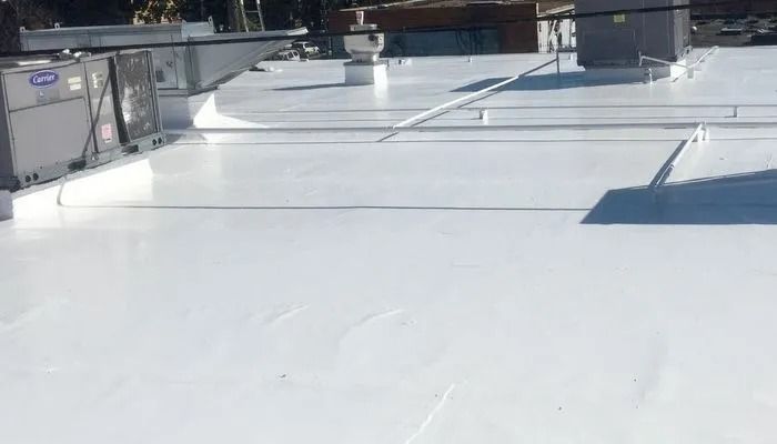 A flat, bright white roof with HVAC units and vents under a clear blue sky.