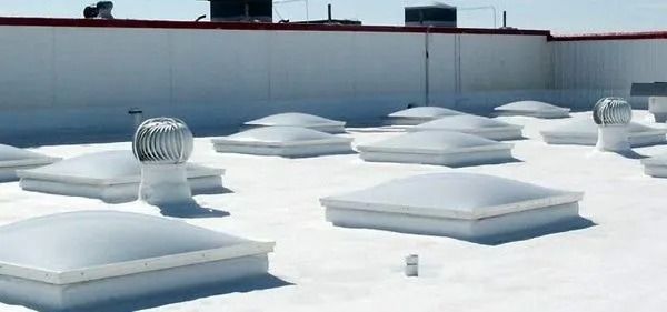 A white, flat commercial roof featuring multiple square skylights and several metallic turbine roof vents.
