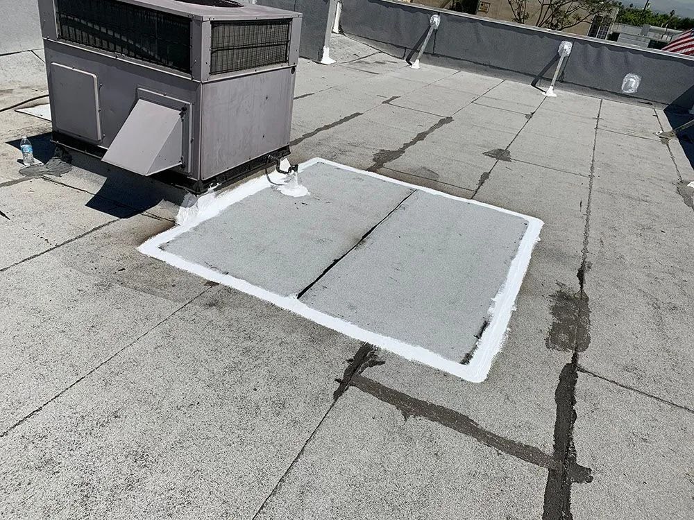 A rooftop HVAC unit sits next to a square roof patch sealed with white waterproof flashing.