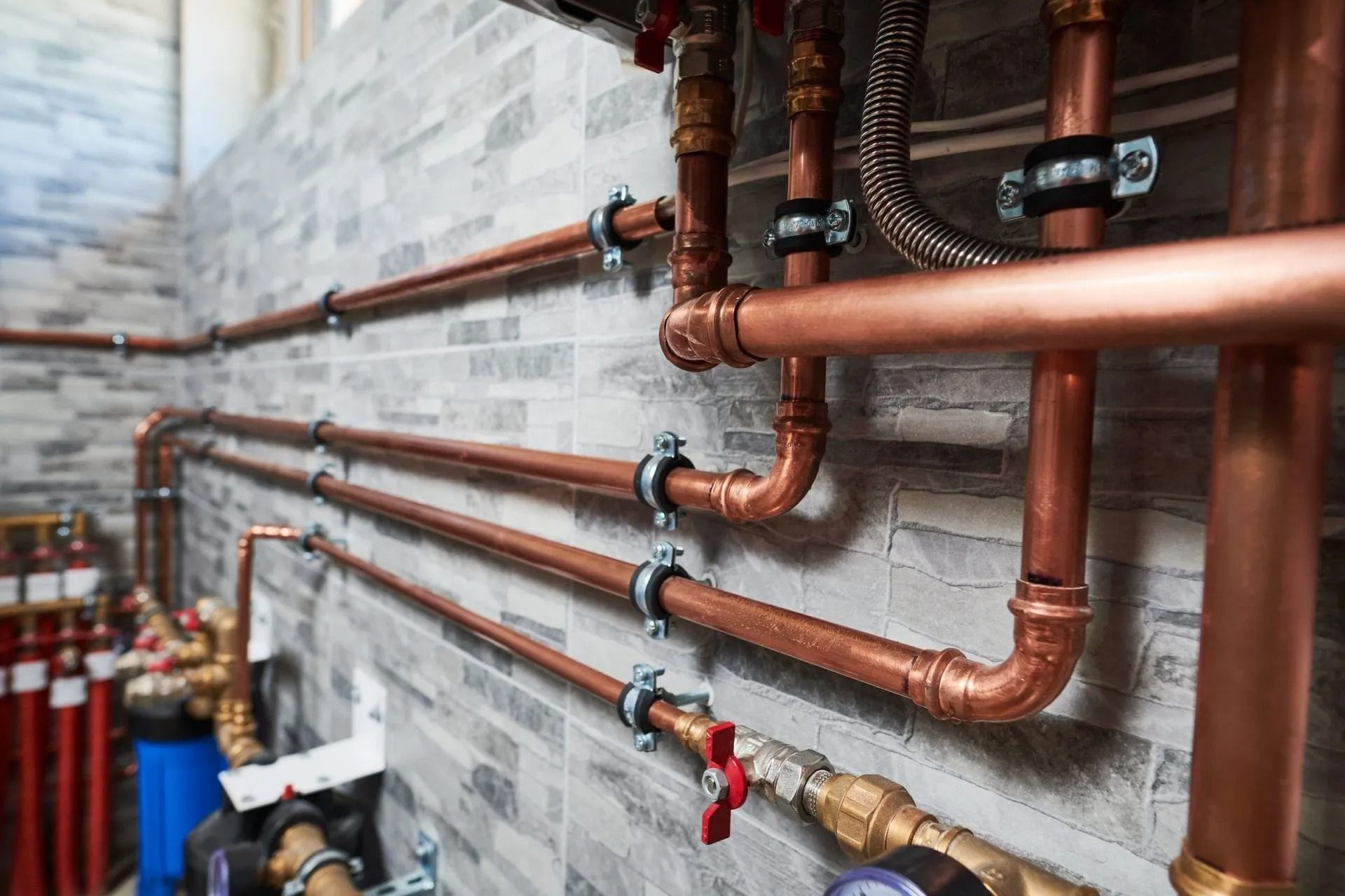 Copper piping and valves mounted on a textured gray tiled wall in a utility or boiler room.