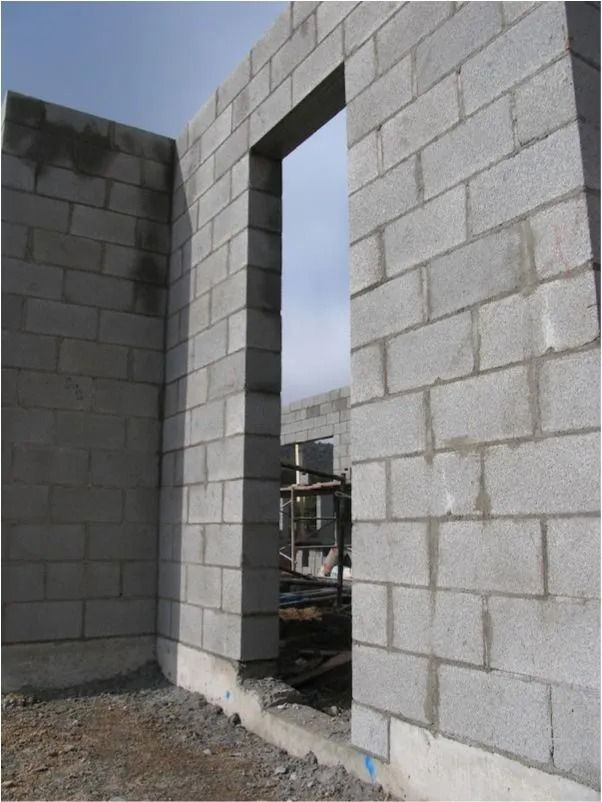 A construction site showing a tall, narrow doorway frame built from gray concrete blocks against a partially finished wall.