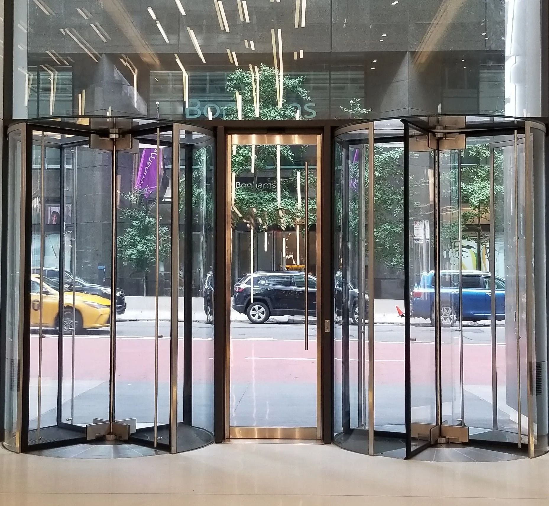 A glass revolving door entryway with a central swinging door, viewed from inside a brightly lit building lobby.