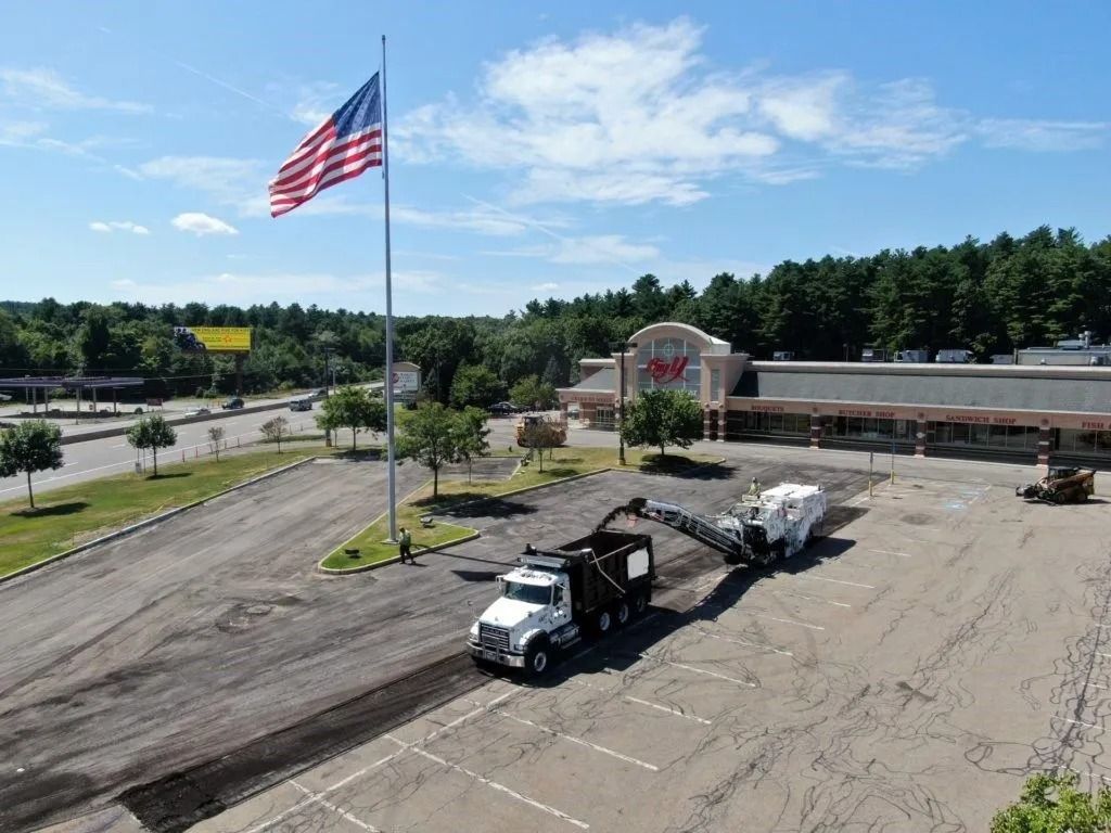 An aerial view of a construction crew milling a commercial parking lot with a truck and equipment near a CVS pharmacy.